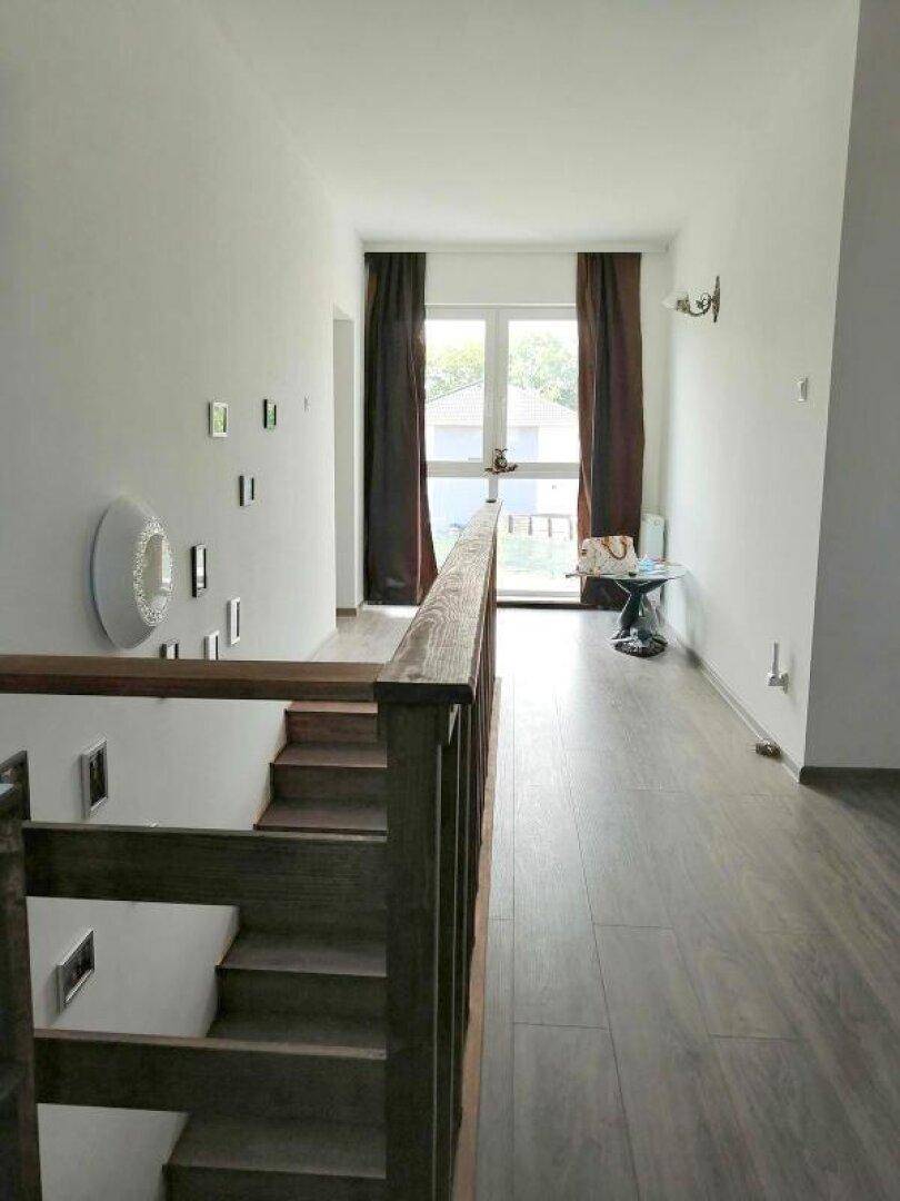 Heller Flur im Obergeschoss mit Holztreppe, Holzoptik-Fliesen und Fenster.