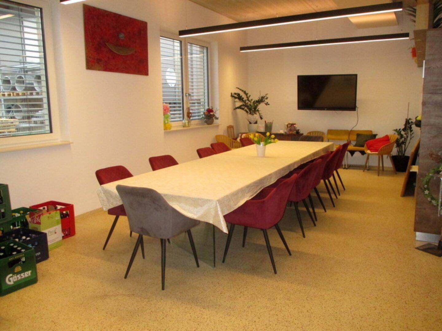 Großer Konferenzraum mit langem Tisch, roten Stühlen und einem Wandfernseher in modernem Ambiente.