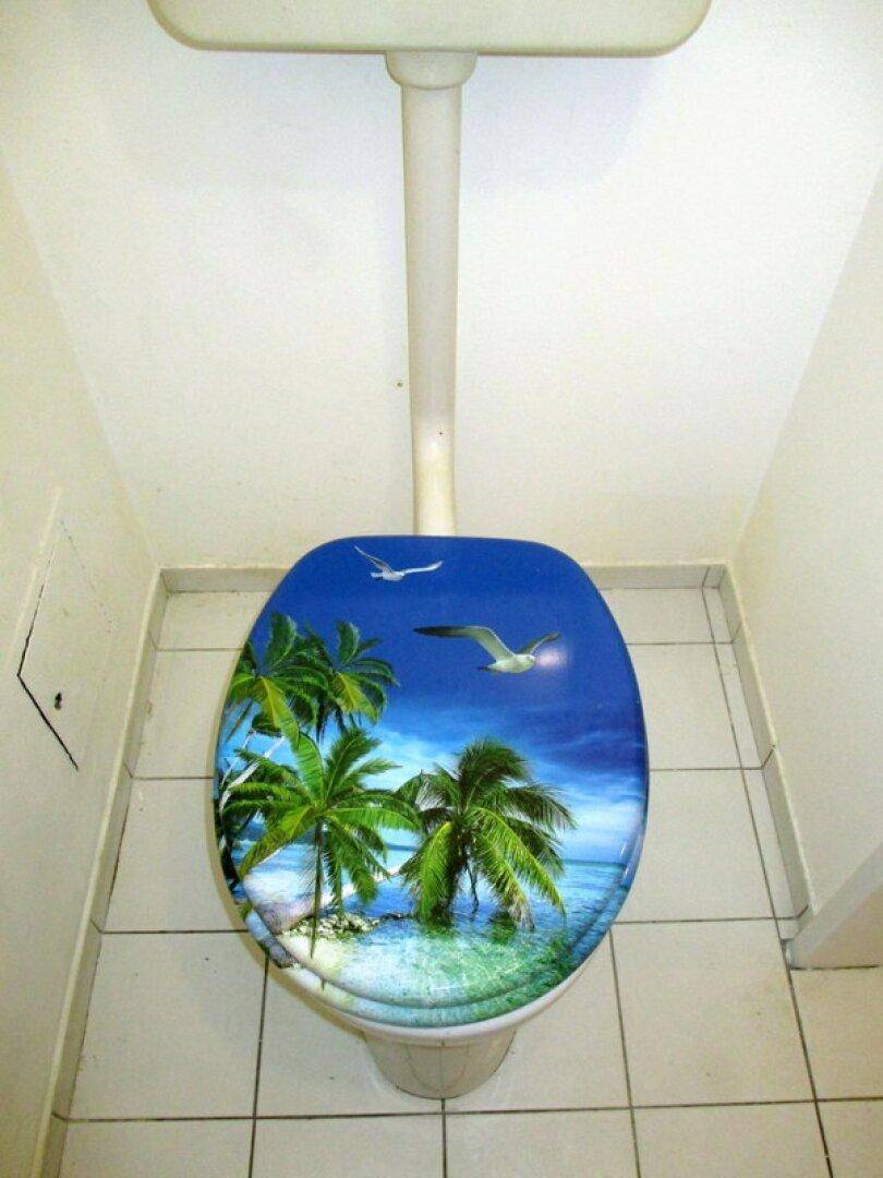 Separate Toilette mit gefliestem Boden und einem dekorativen Toilettendeckel mit Palmenmotiv.