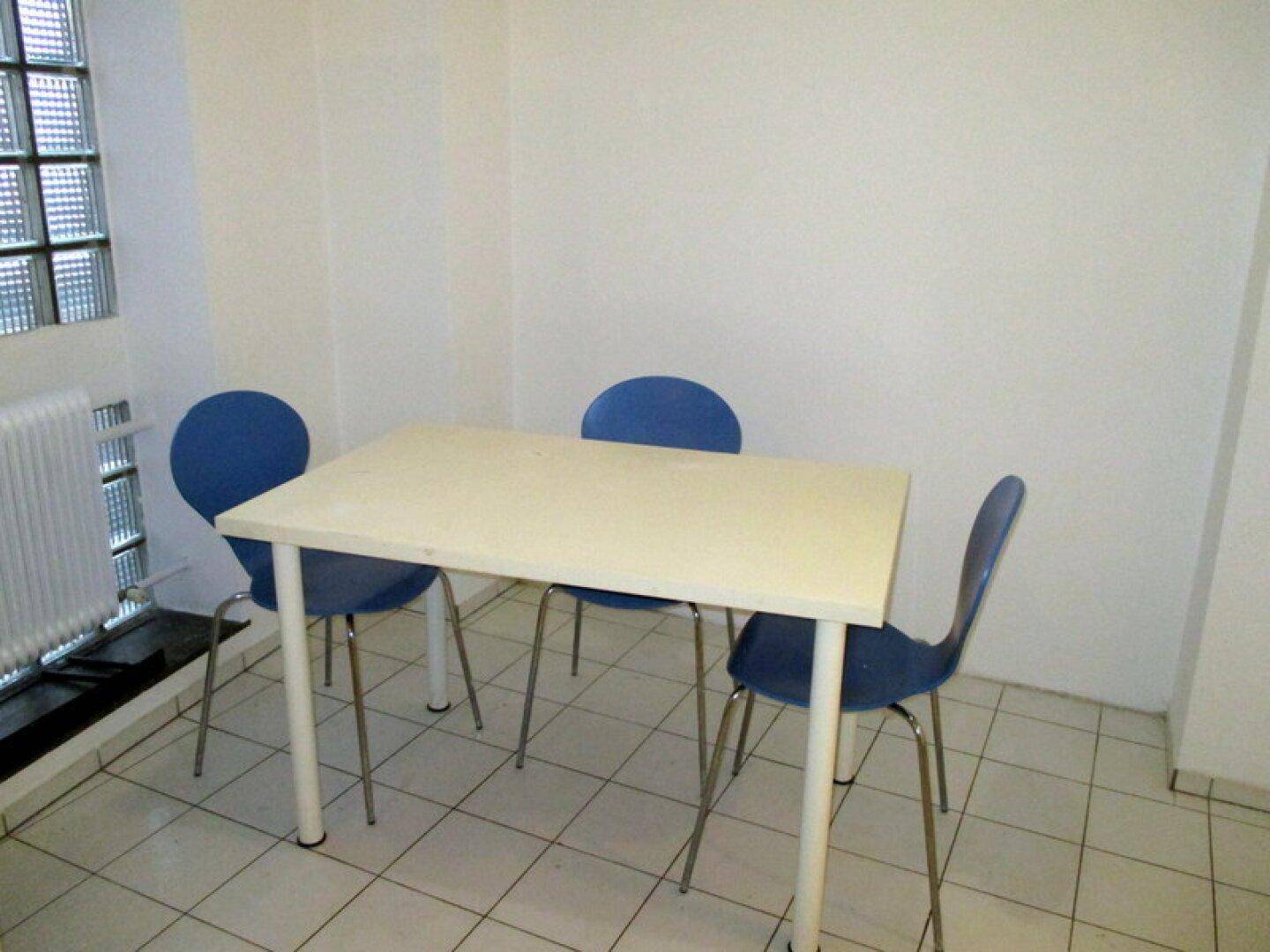 Kleiner Essbereich mit einem Tisch und blauen Stühlen auf einem gefliesten Boden.