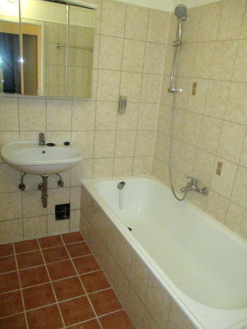 Badezimmer mit Badewanne, Waschbecken und beigefarbenen Wandfliesen sowie Terrakotta-Bodenfliesen.