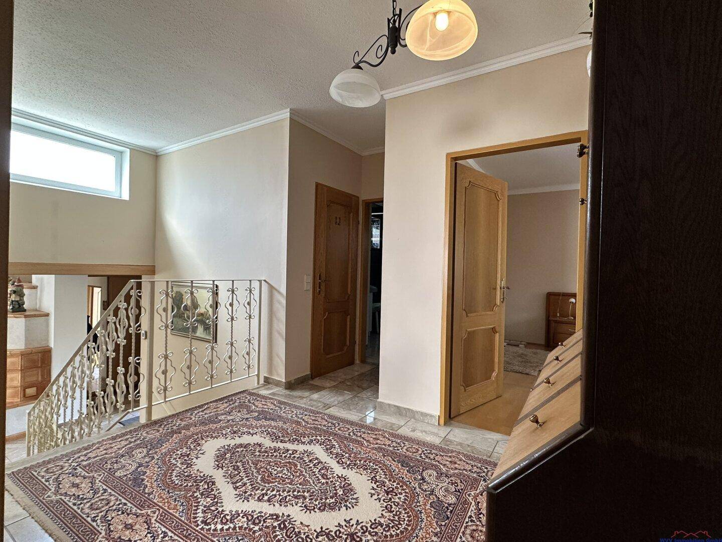 Heller Flur im Obergeschoss mit Teppich, schmiedeeisernem Geländer und Holztüren.