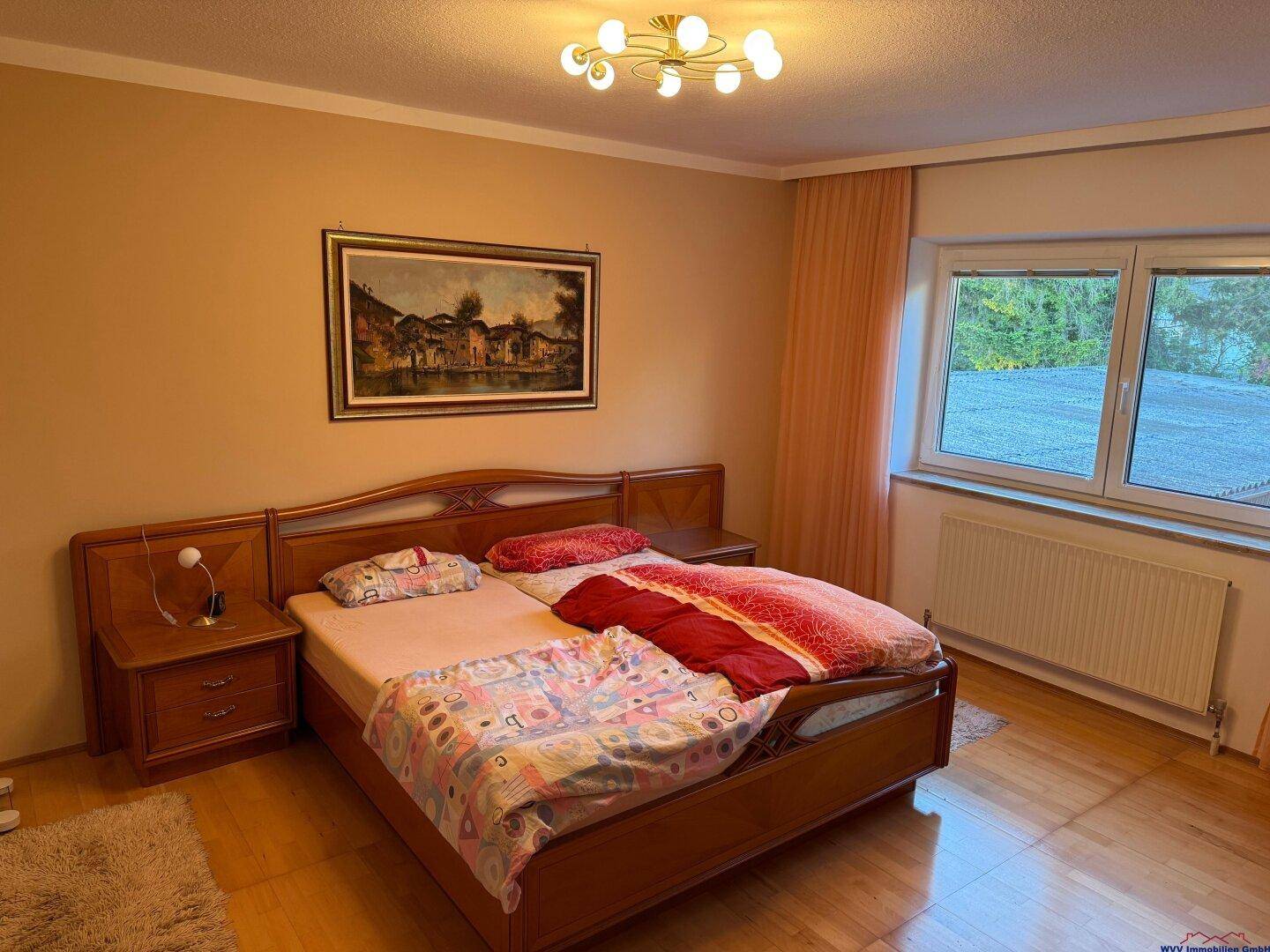 Gemütliches Schlafzimmer mit Holzbett, Parkettboden und Fenster mit Blick ins Grüne.