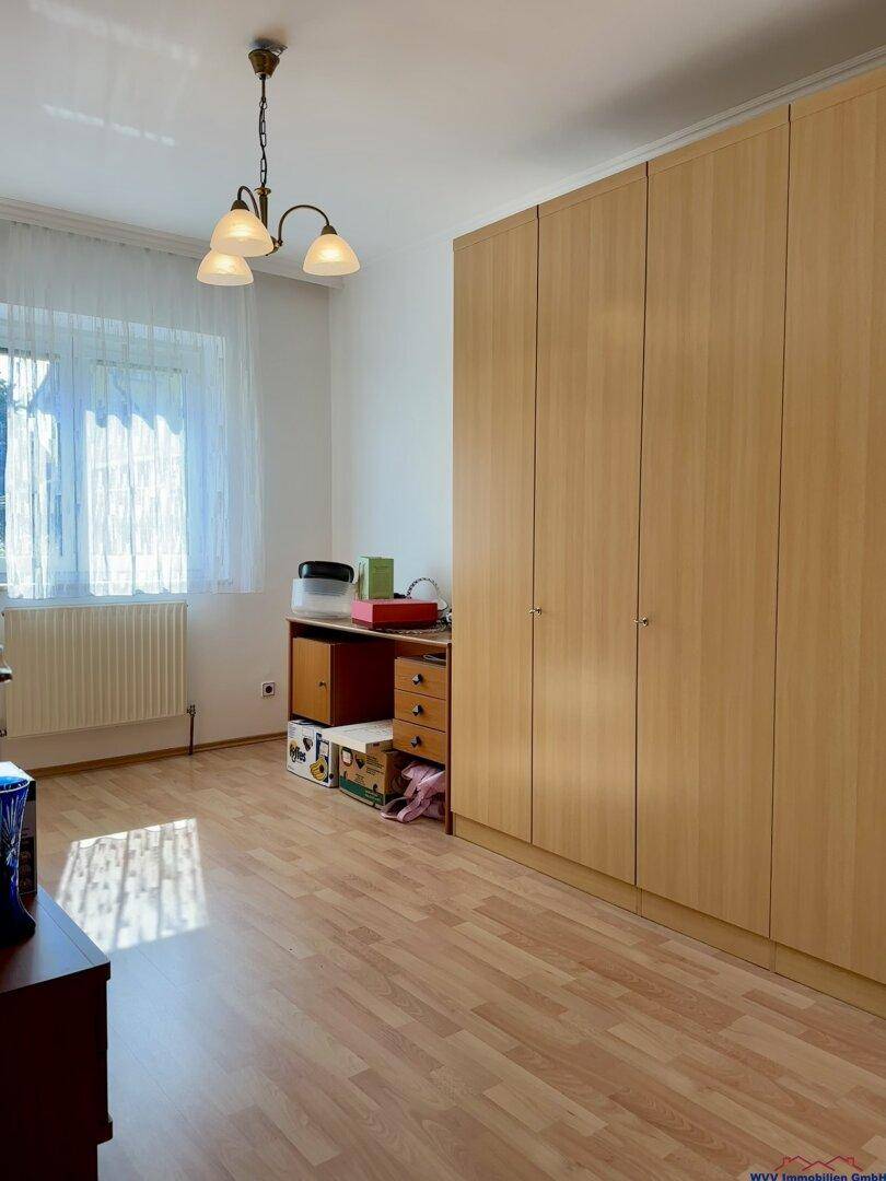 Schlafzimmer mit Laminatboden, Einbauschränken und Schreibtisch am Fenster.