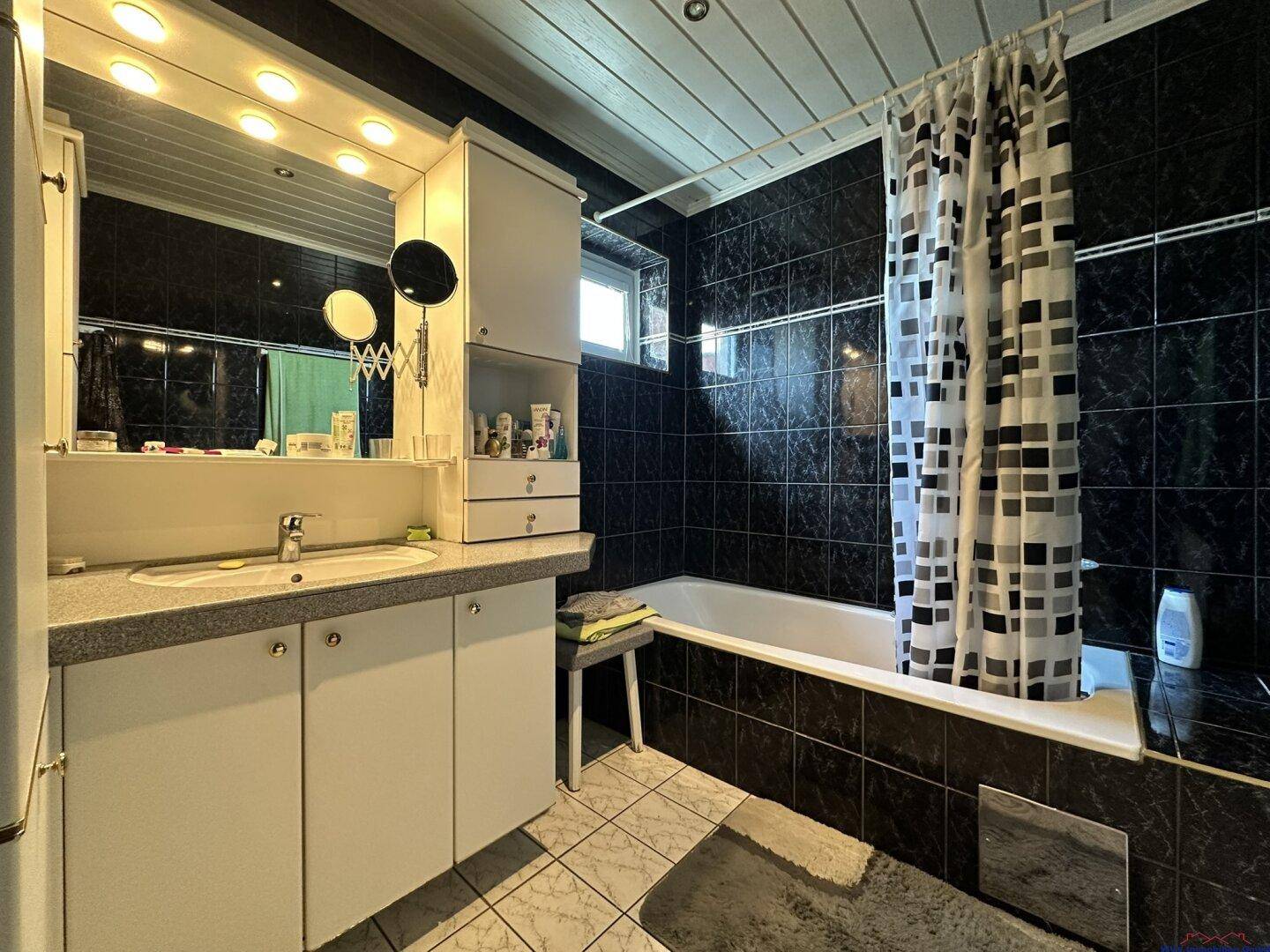 Badezimmer mit dunklen Fliesen, Badewanne mit Duschvorhang und Einzelwaschbecken.