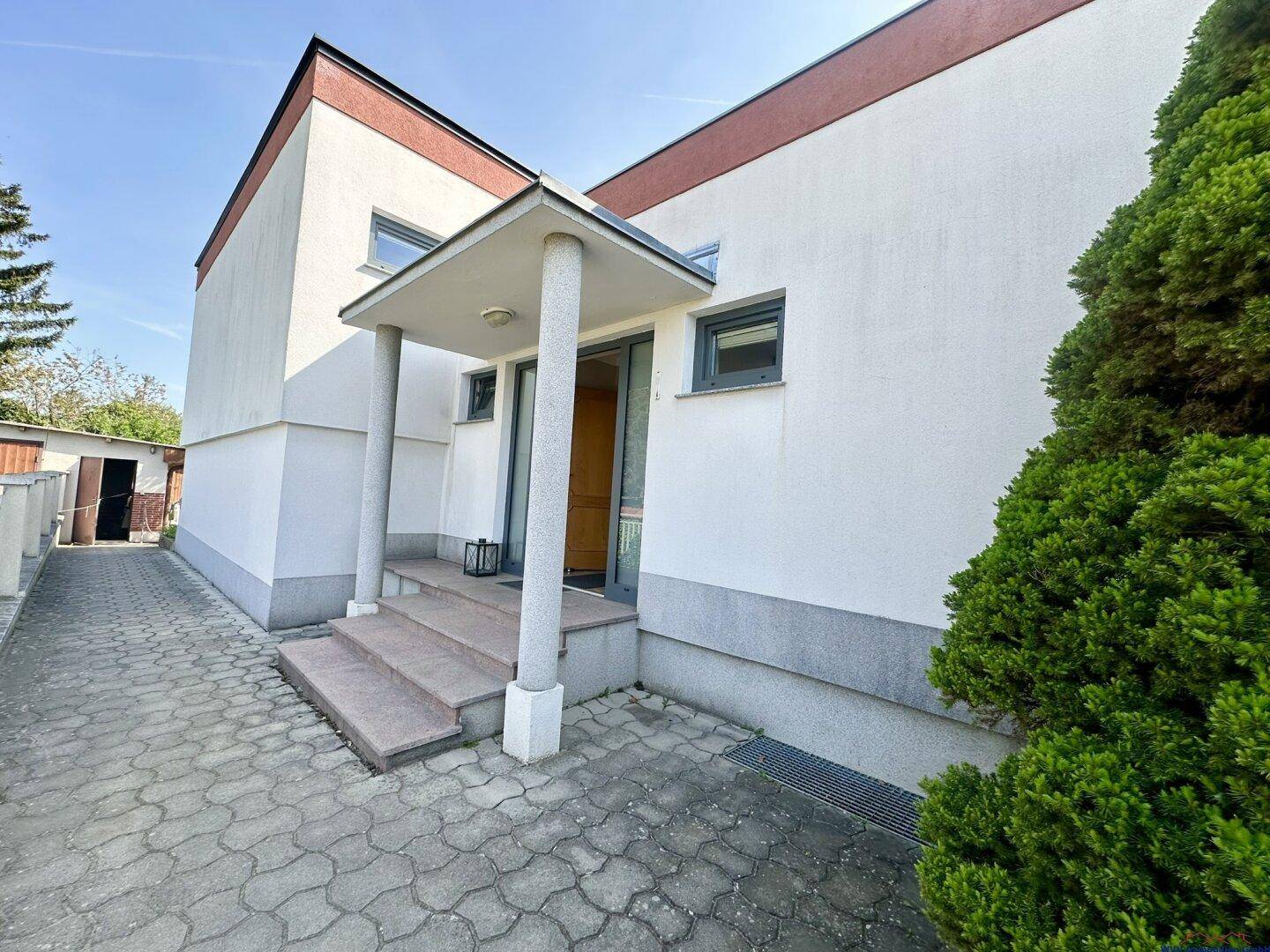 Eingangsbereich des Hauses mit überdachtem Portikus und gepflastertem Zugang.