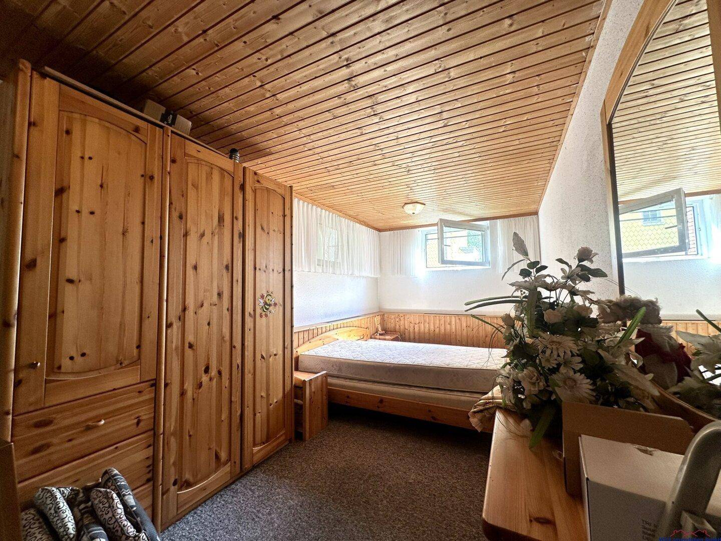 Gemütliches Zimmer im Untergeschoss mit Holzdecke, Teppichboden und kleinem Fenster.