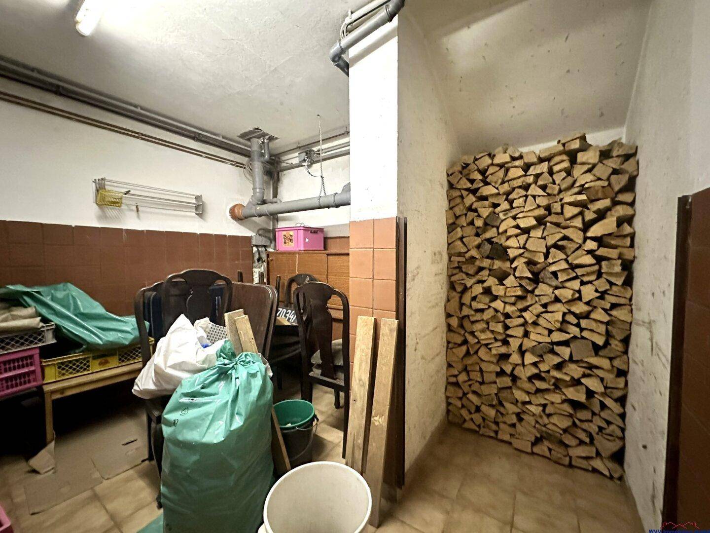 Kellerraum zur Lagerung von Brennholz mit gestapelten Holzscheiten und Stauraum.
