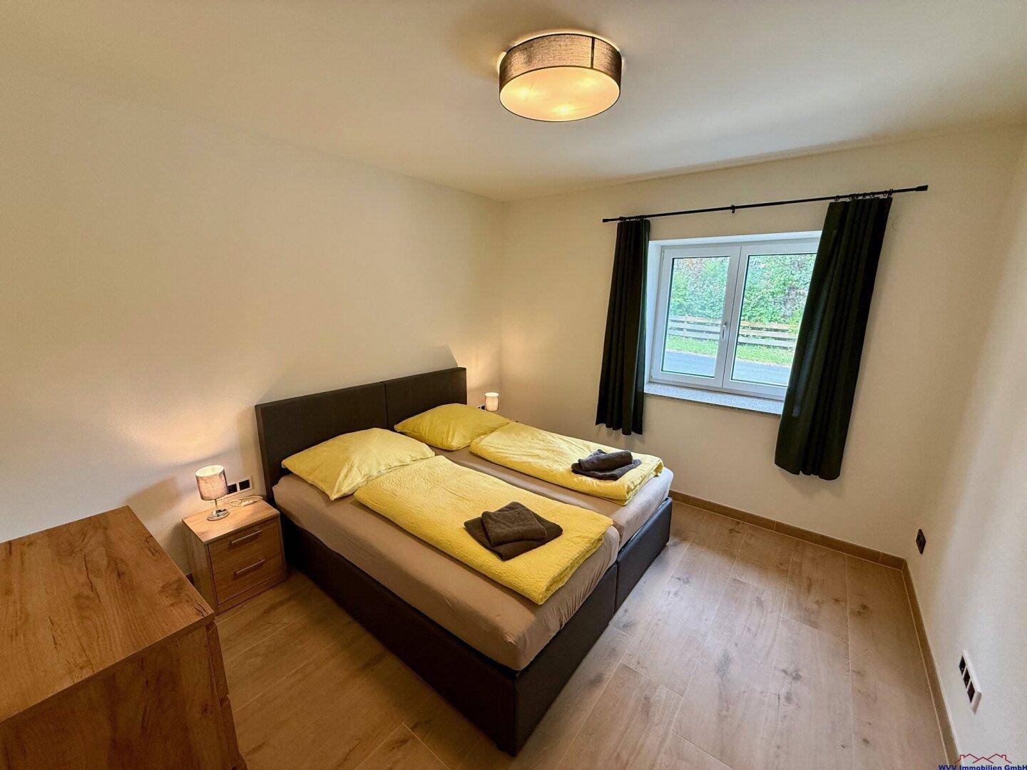 Helles Schlafzimmer mit zwei Einzelbetten, Holzboden und einem Nachttisch mit Lampe.