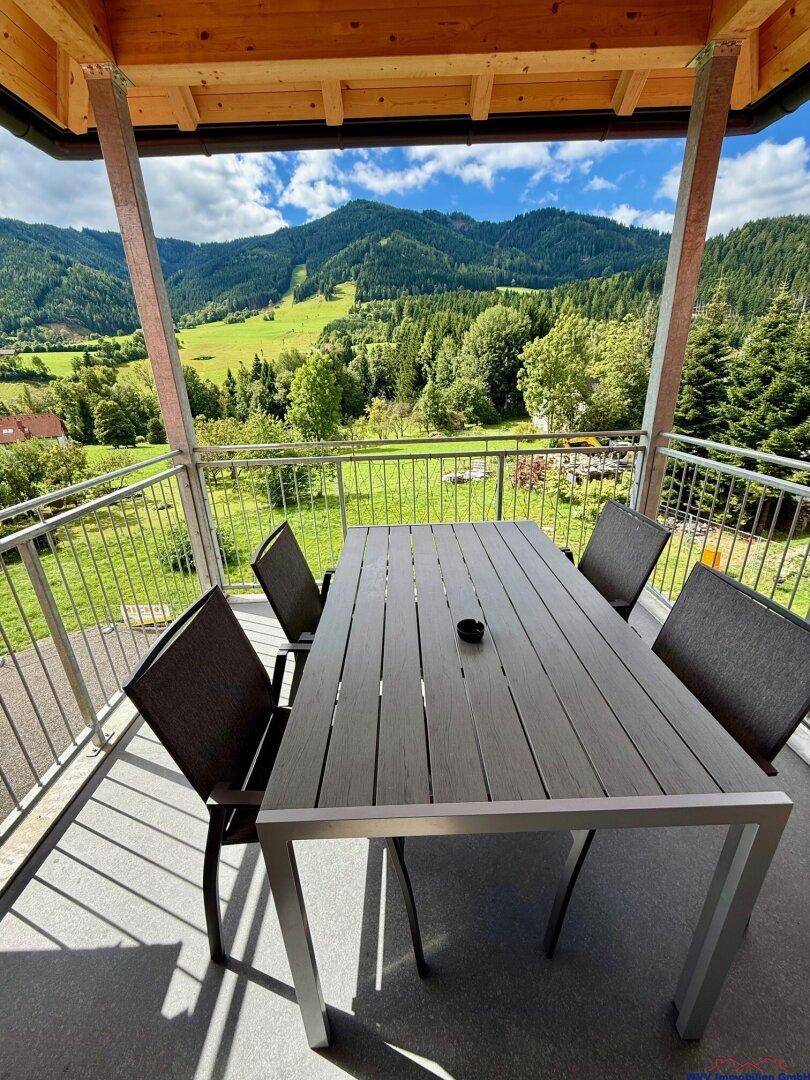 Geräumiger Balkon mit Esstisch und Stühlen, bietet einen weiten Blick auf die grüne Berglandschaft.