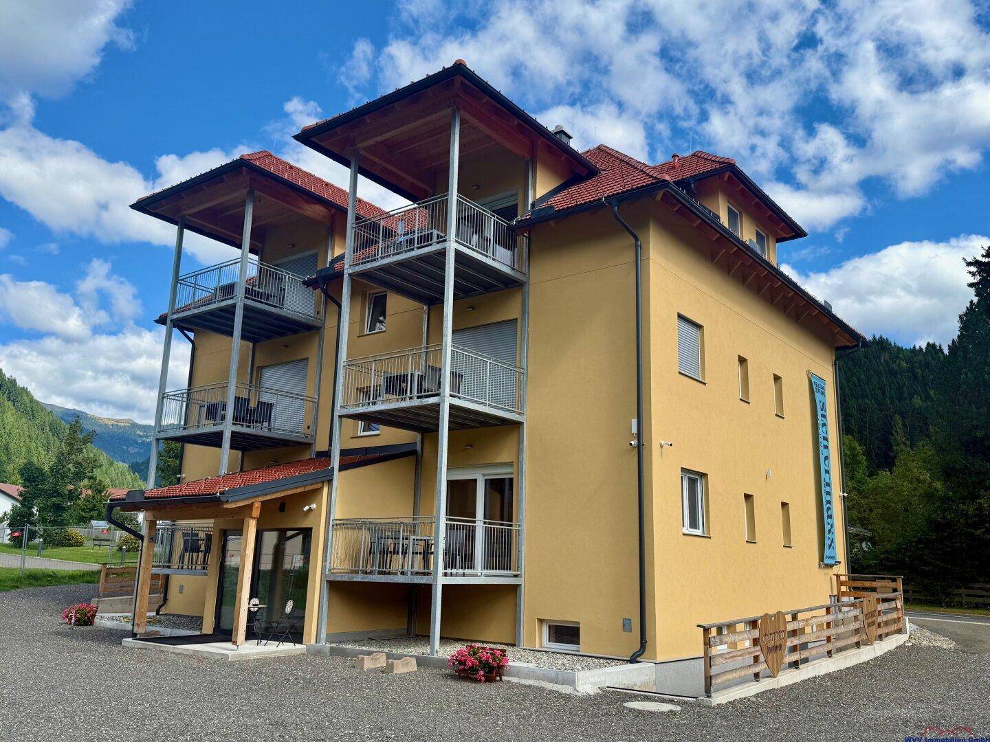 Modernes Apartmenthaus mit gelber Fassade, Holzelementen und mehreren Balkonen unter blauem Himmel.