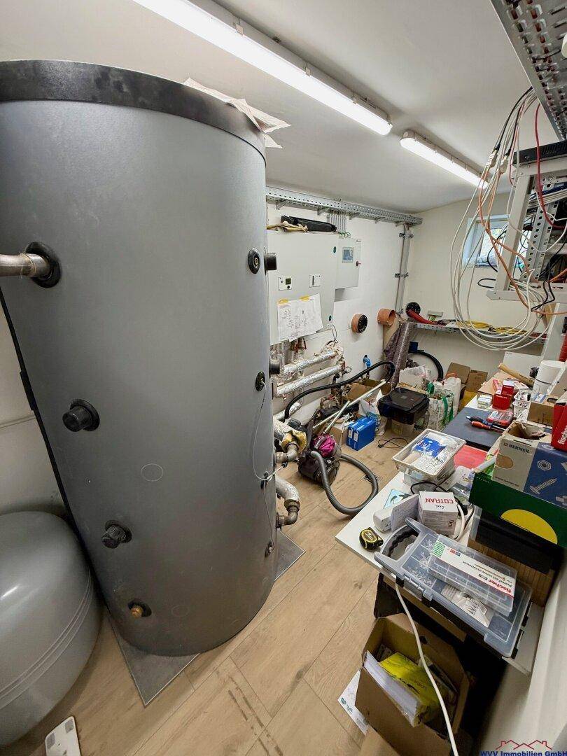 Technikraum mit großem Warmwasserspeicher, Rohren und elektrischen Installationen.