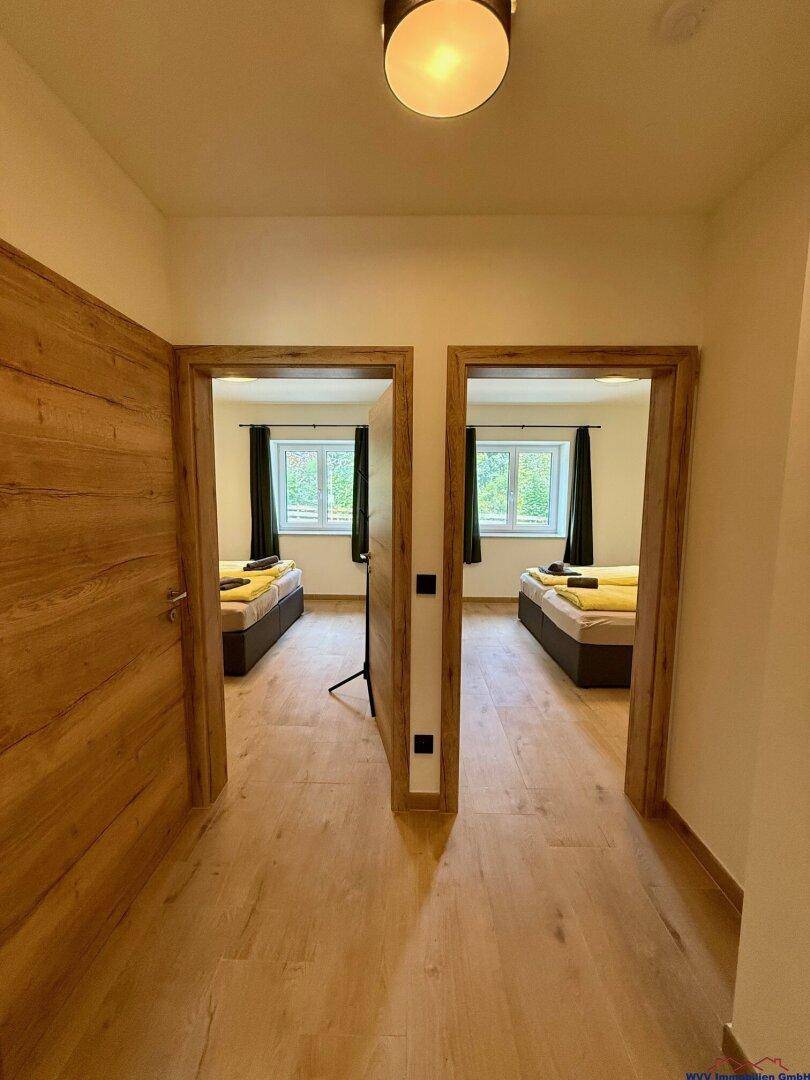 Heller Flur mit Holzboden, der zu zwei Schlafzimmern mit Einzelbetten führt.