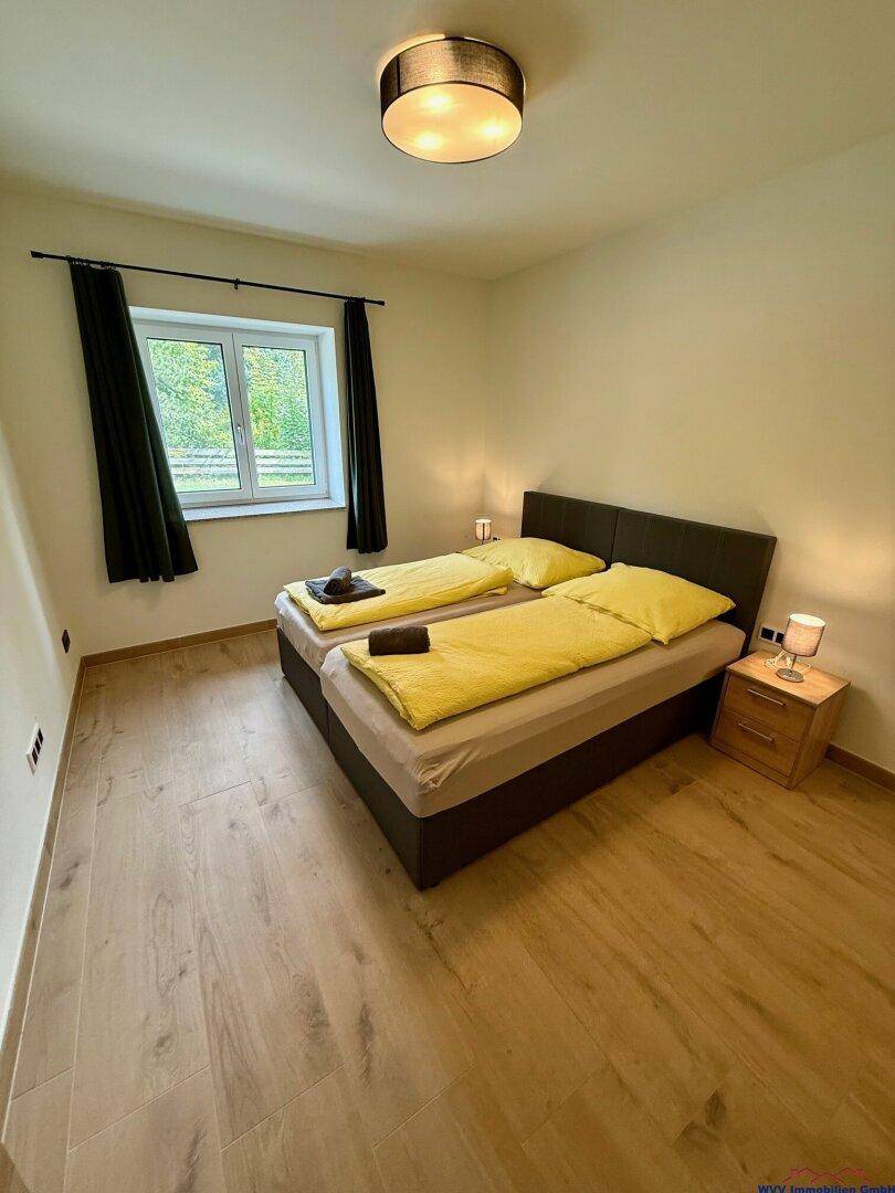 Gemütliches Schlafzimmer mit zwei Einzelbetten, Holzboden und einem Fenster mit Blick ins Grüne.