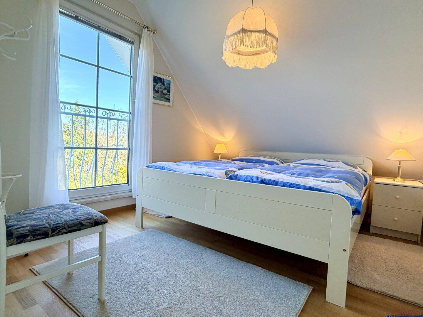Helles Schlafzimmer im Dachgeschoss mit Holzbett und großem Fenster.