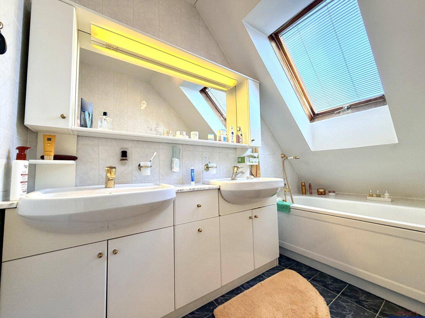 Badezimmer im Dachgeschoss mit Doppelwaschbecken, Badewanne und Dachfenster.