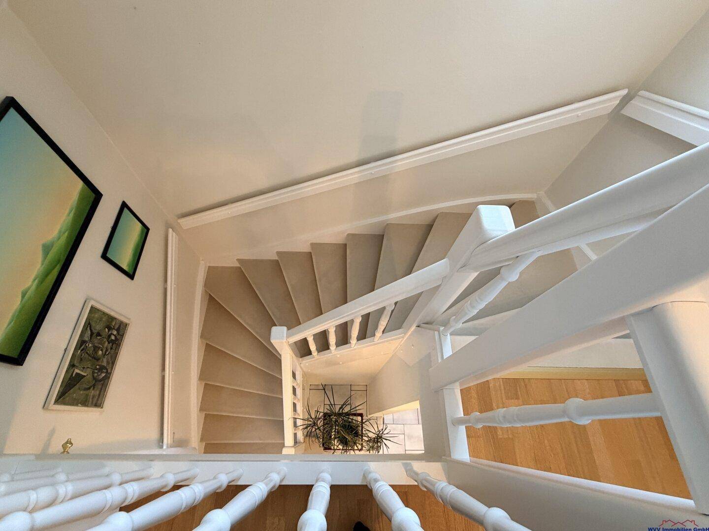 Wendeltreppe mit Teppichstufen und weißem Geländer, die die Etagen verbindet.