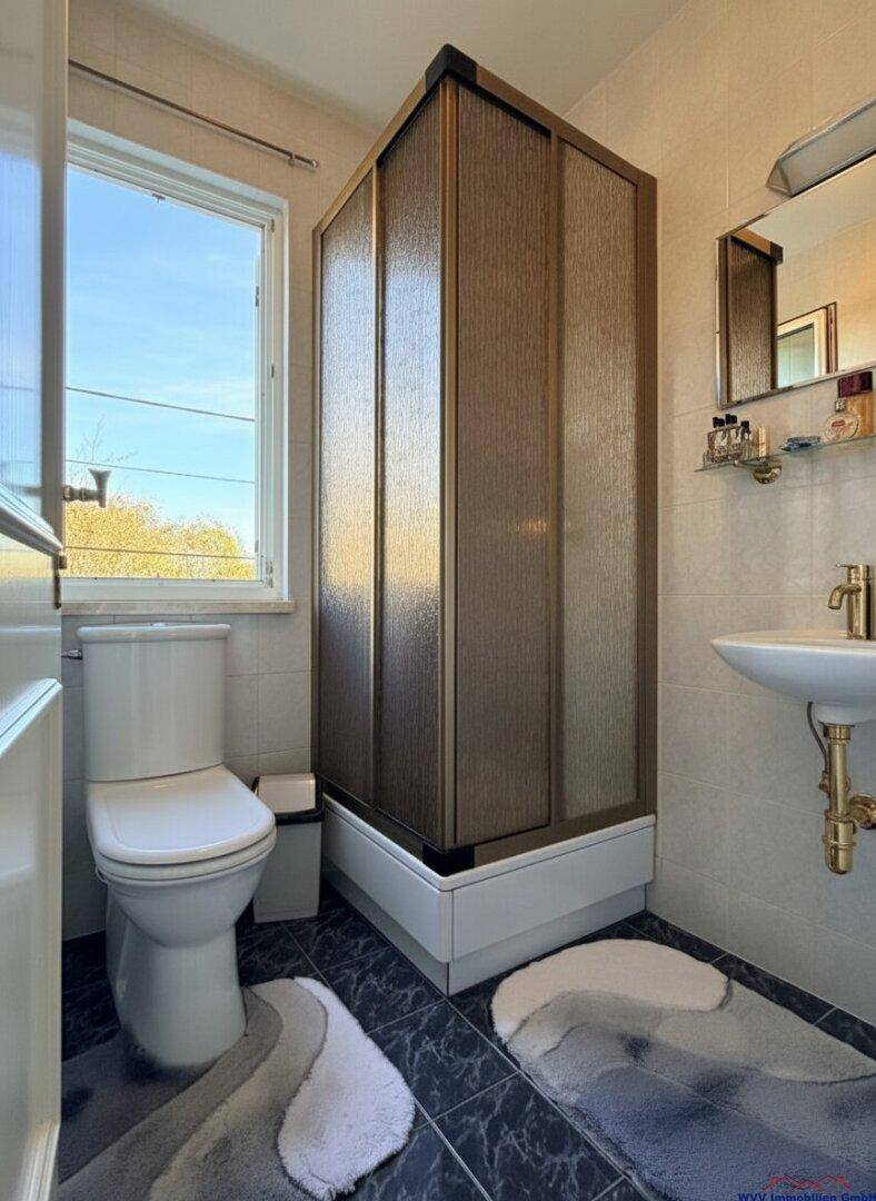 Badezimmer mit Duschkabine, WC, Waschbecken und Fenster für Tageslicht.