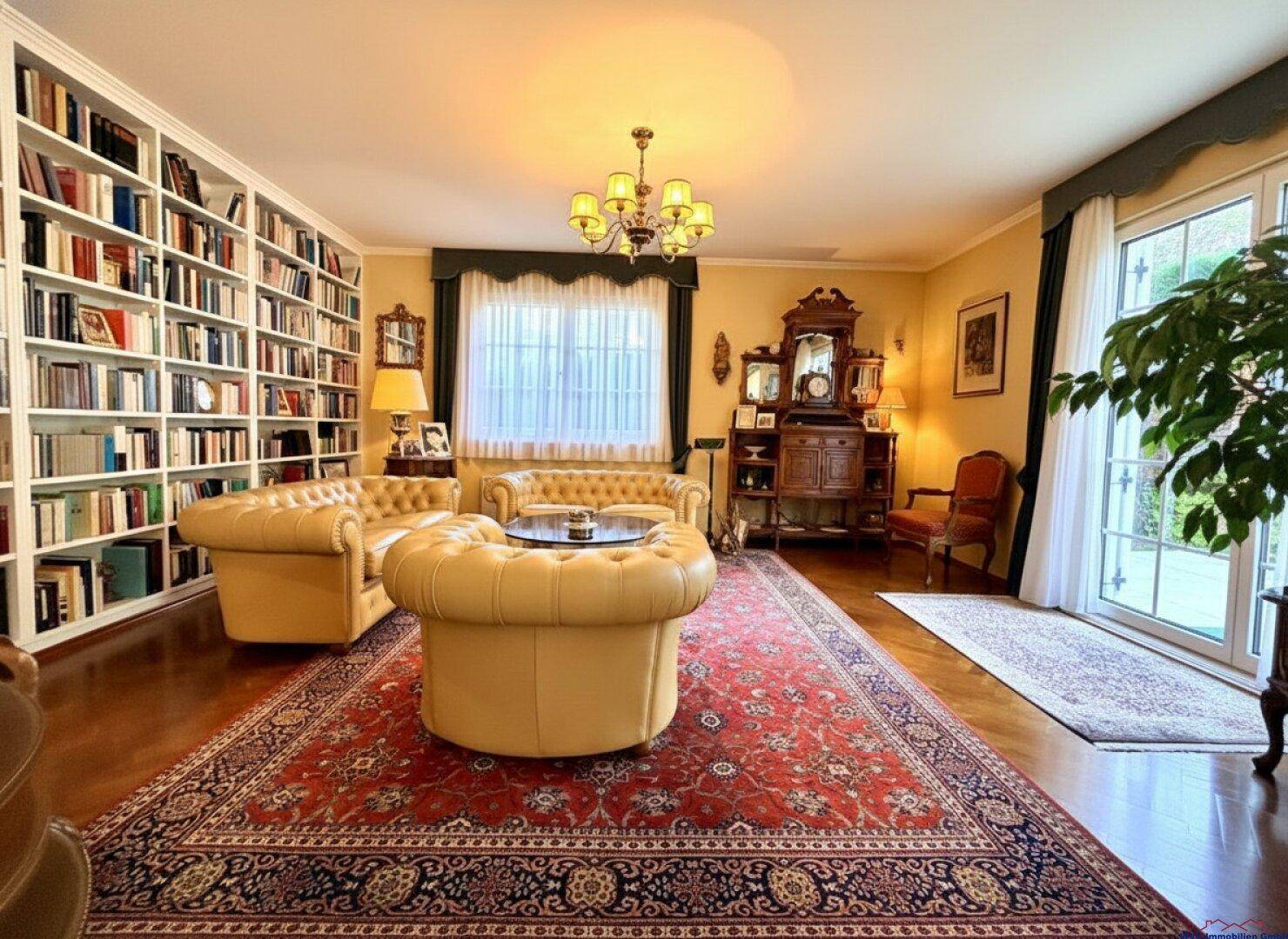 Geräumiges Wohnzimmer mit Bücherwand, Chesterfield-Möbeln und Zugang zur Terrasse.