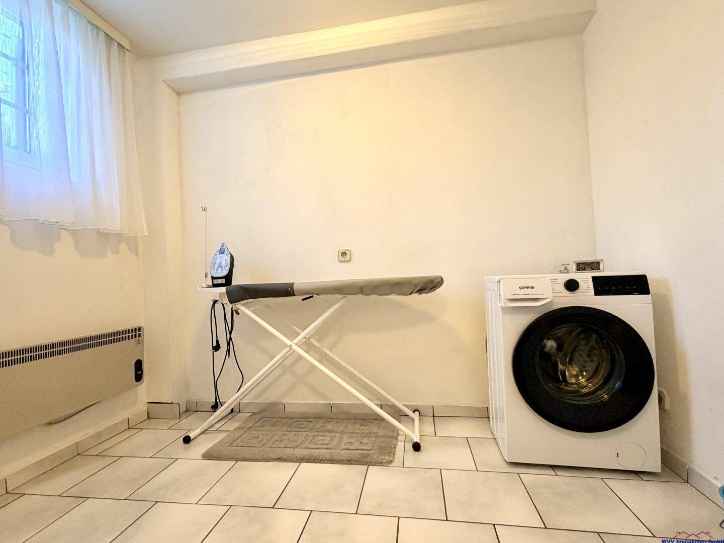 Praktischer Waschraum mit Waschmaschine, Bügelbrett und Fliesenboden.