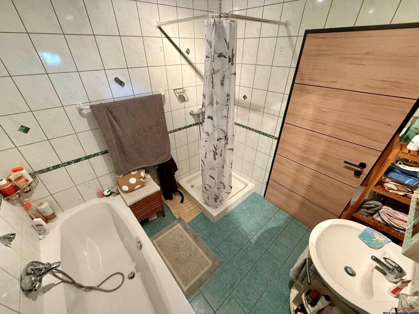 Badezimmer mit Badewanne, Duschbereich und Fliesen in Weiß und Türkis.