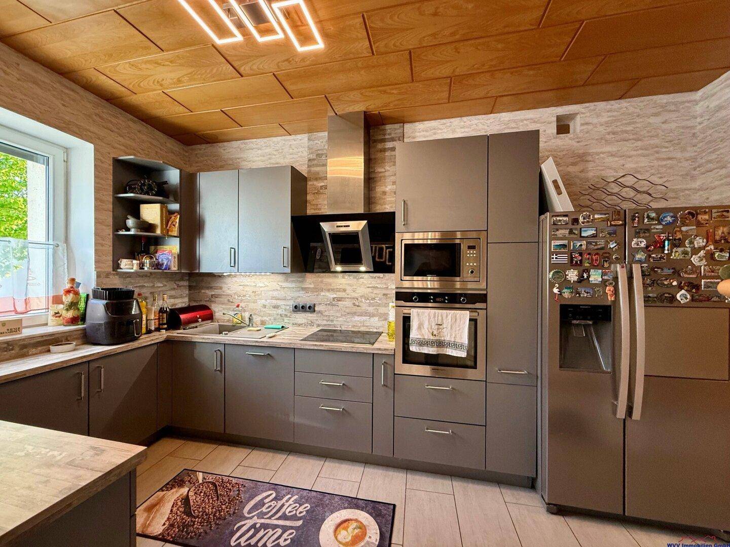 Moderne Küche mit grauen Schränken, Einbaugeräten und einem großen Kühlschrank.