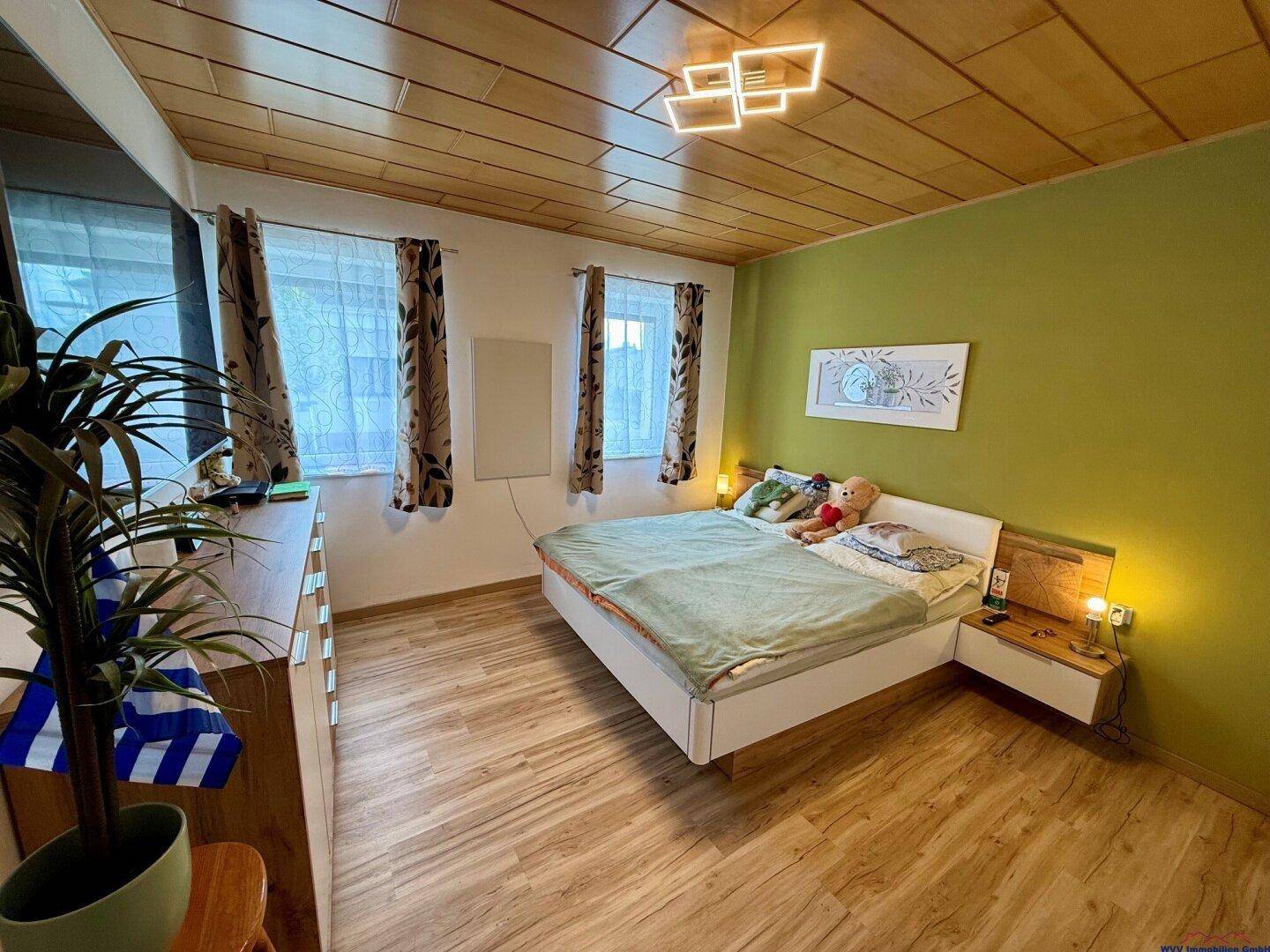 Schlafzimmer mit Holzboden, grüner Akzentwand und einem Doppelbett mit Nachttischen.