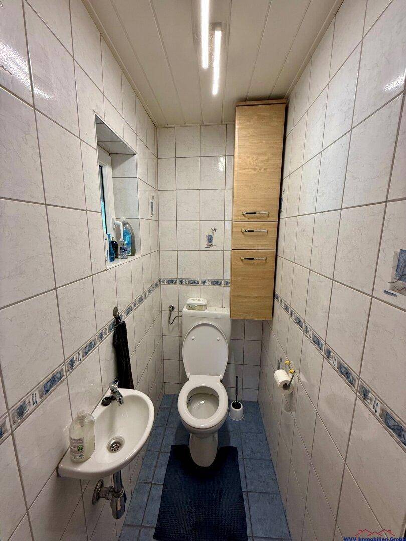 Kleines Gäste-WC mit Toilette, Waschbecken und weißen Fliesen mit blauer Bordüre.