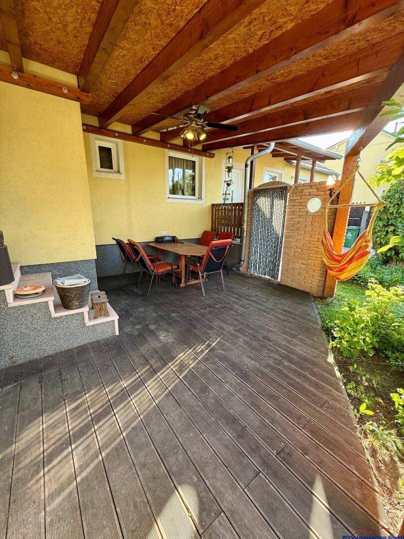 Überdachte Holzterrasse mit Esstisch und Stühlen, ideal für Mahlzeiten im Freien.