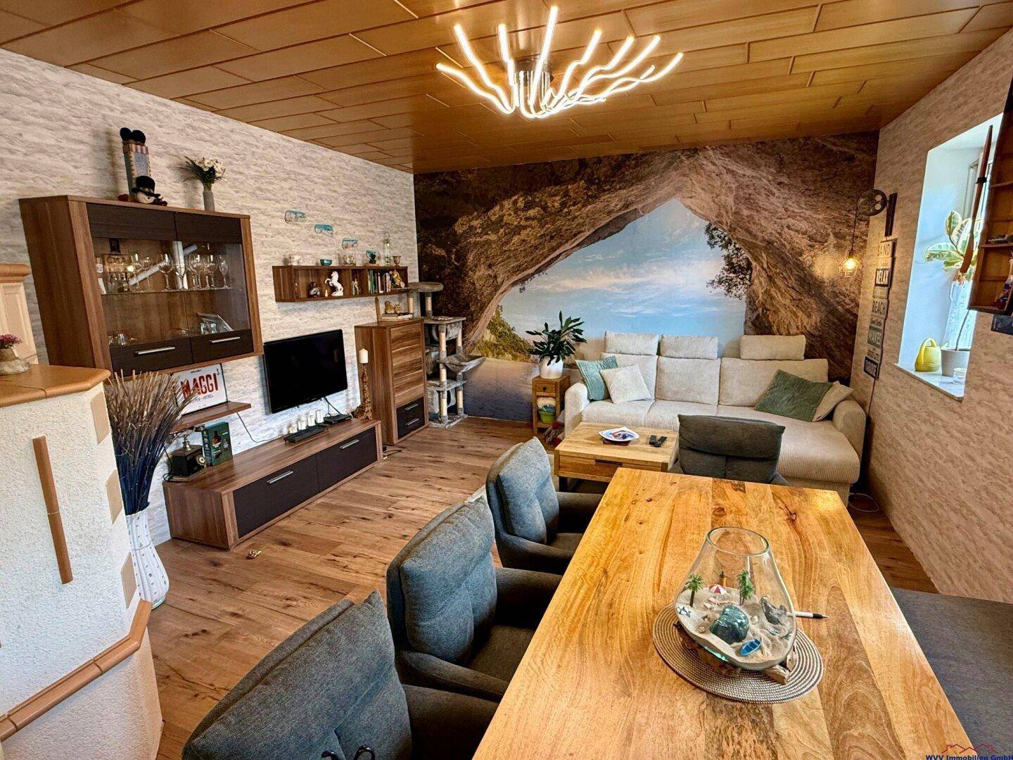 Gemütlicher Wohn-Essbereich mit Holzboden, großem Esstisch und einer modernen Couch.