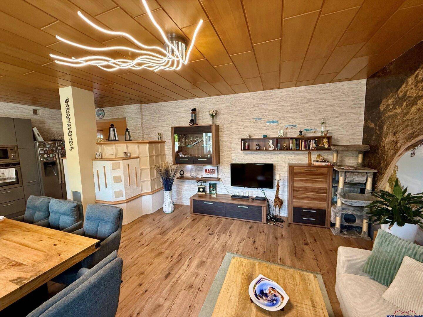 Offener Wohnbereich mit Holzboden, stilvoller Deckenbeleuchtung und einem Kachelofen.