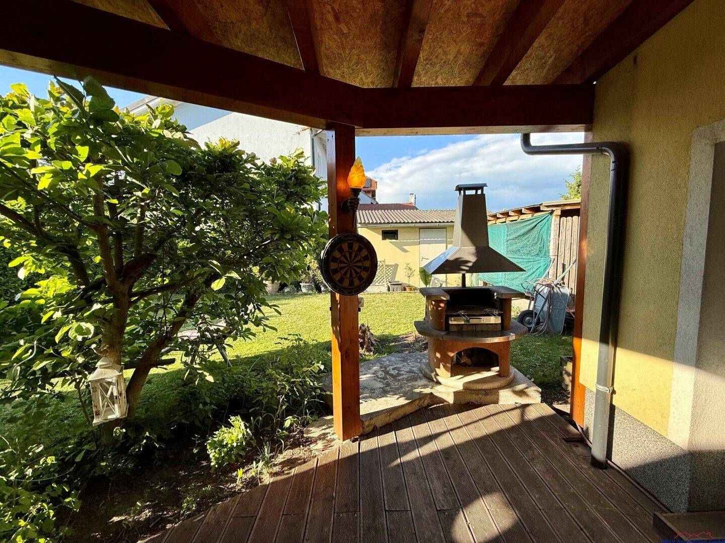Überdachter Terrassenbereich mit eingebautem Grill und Blick auf den Garten.