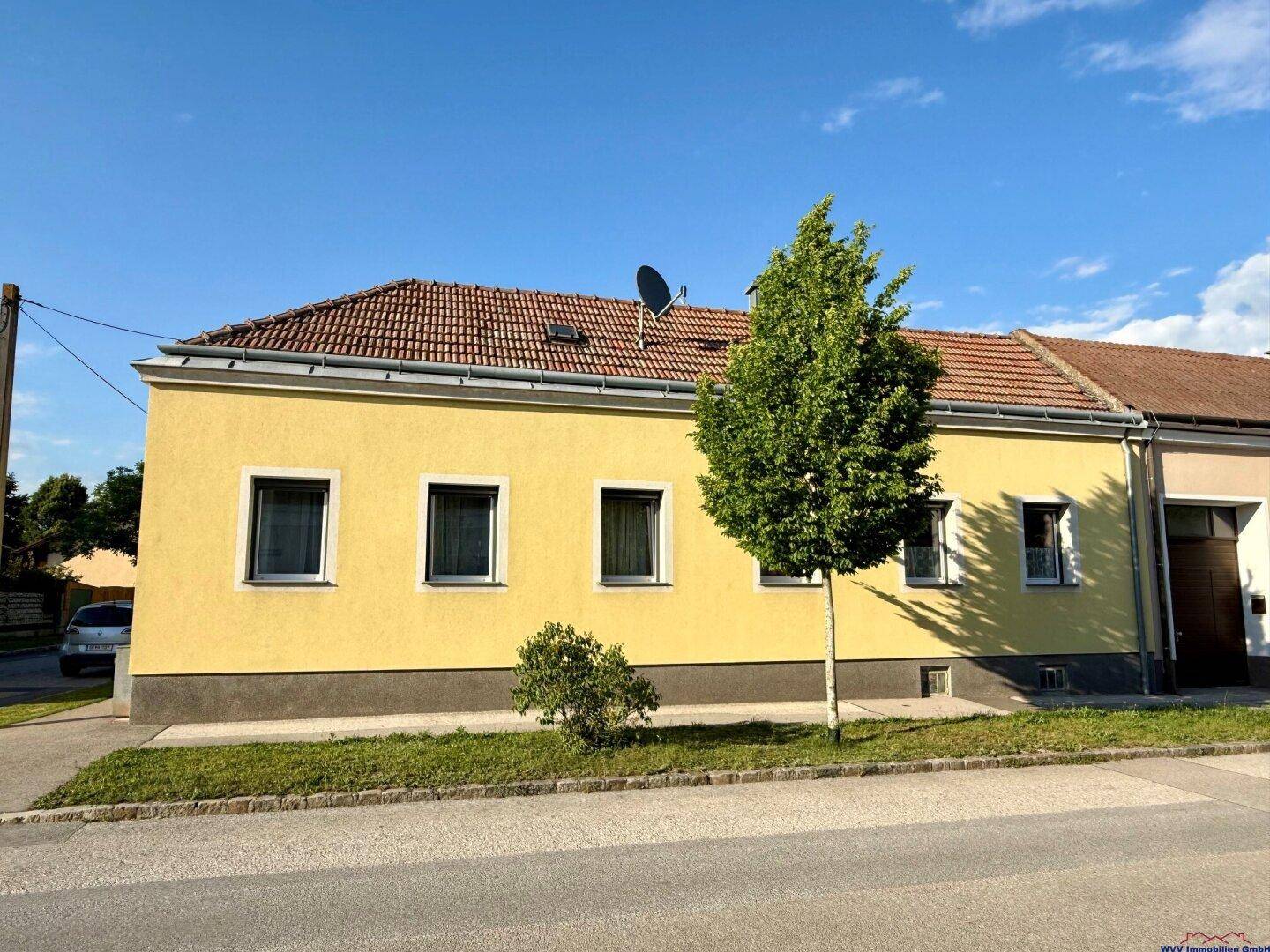 Vorderansicht des Hauses mit gelber Fassade, Ziegeldach und einem Baum vor den Fenstern.
