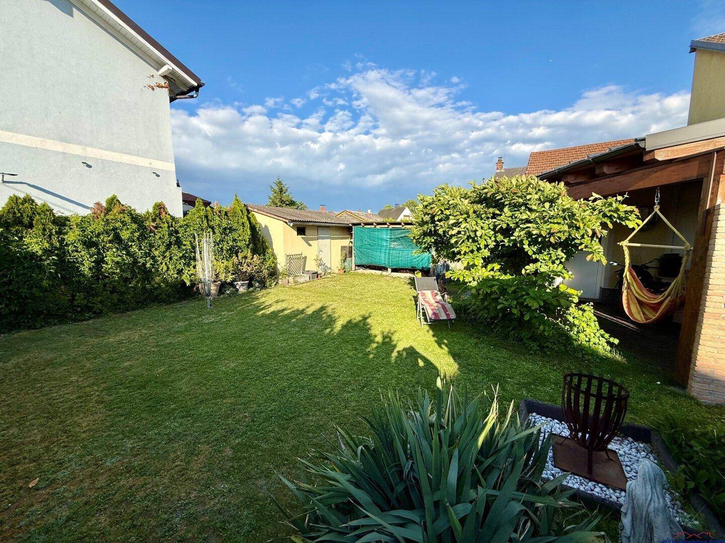 Großer, gepflegter Garten mit Rasenfläche, hohen Hecken und einer Hängematte im Schatten.