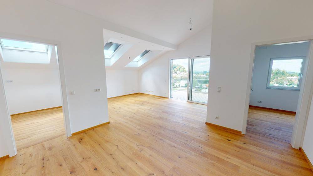 Geräumiger Wohnbereich mit Holzboden, Dachschrägen, Oberlichtern und Zugang zu einem Außenbereich.
