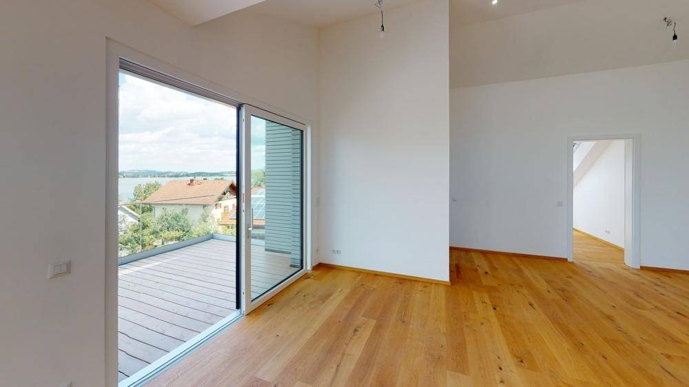 Heller Wohnraum mit Holzboden, großer Schiebetür und Zugang zu einem Balkon mit Seeblick.