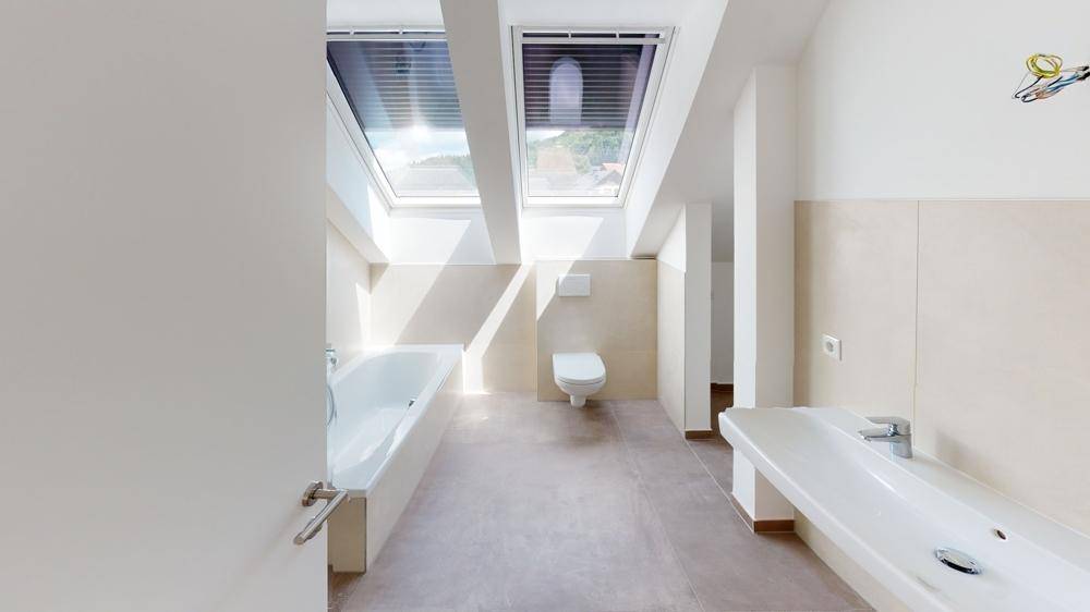 Modernes Badezimmer mit Badewanne, wandhängendem WC, Einzelwaschbecken und zwei Dachfenstern.