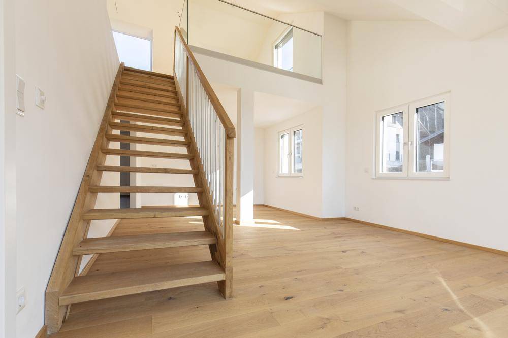 Heller Eingangsbereich mit moderner Holztreppe, Glasgeländer und Holzboden.