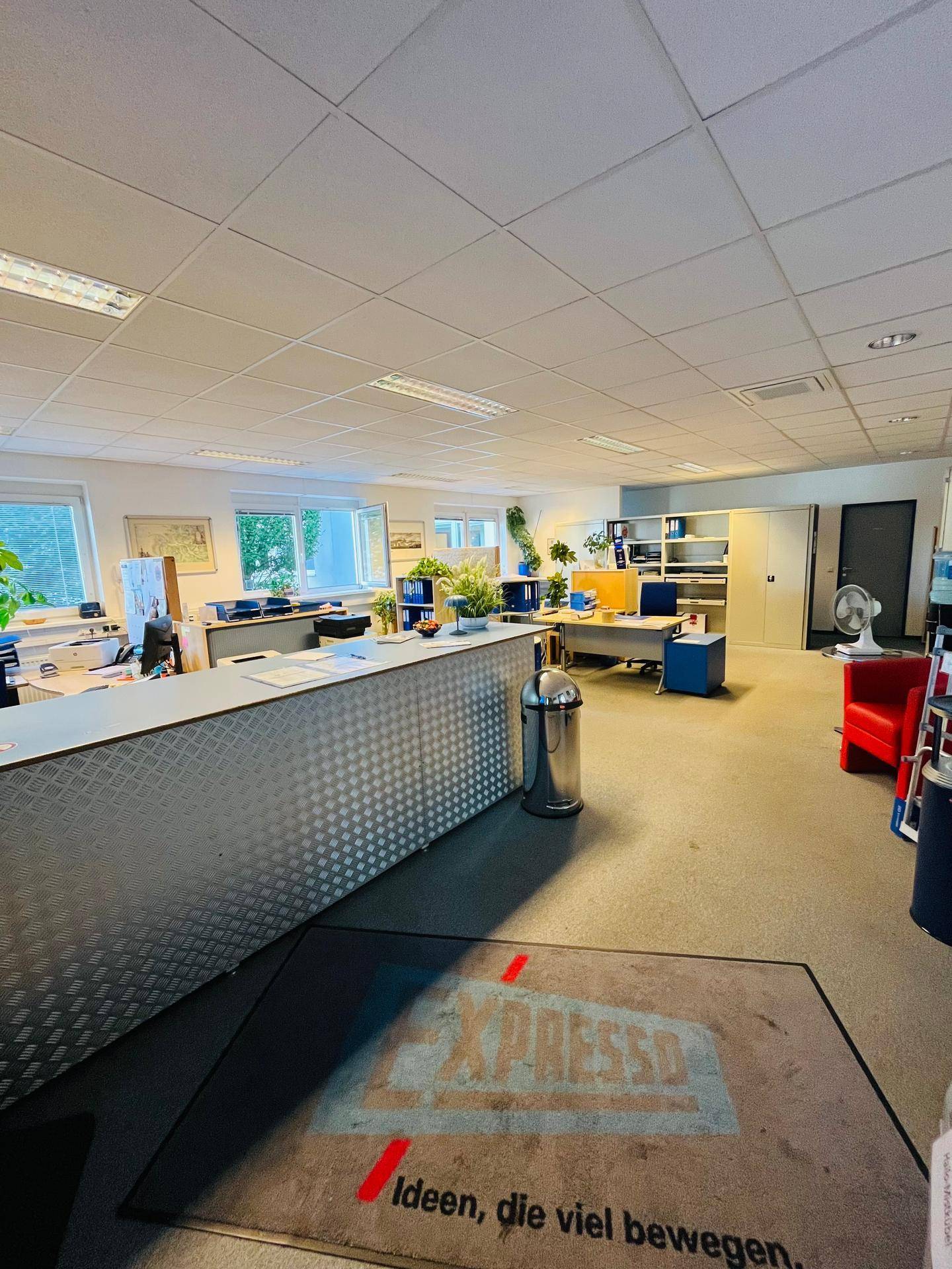 Empfangsbereich eines Großraumbüros mit Theke, Teppichboden und Blick auf weitere Arbeitsplätze.