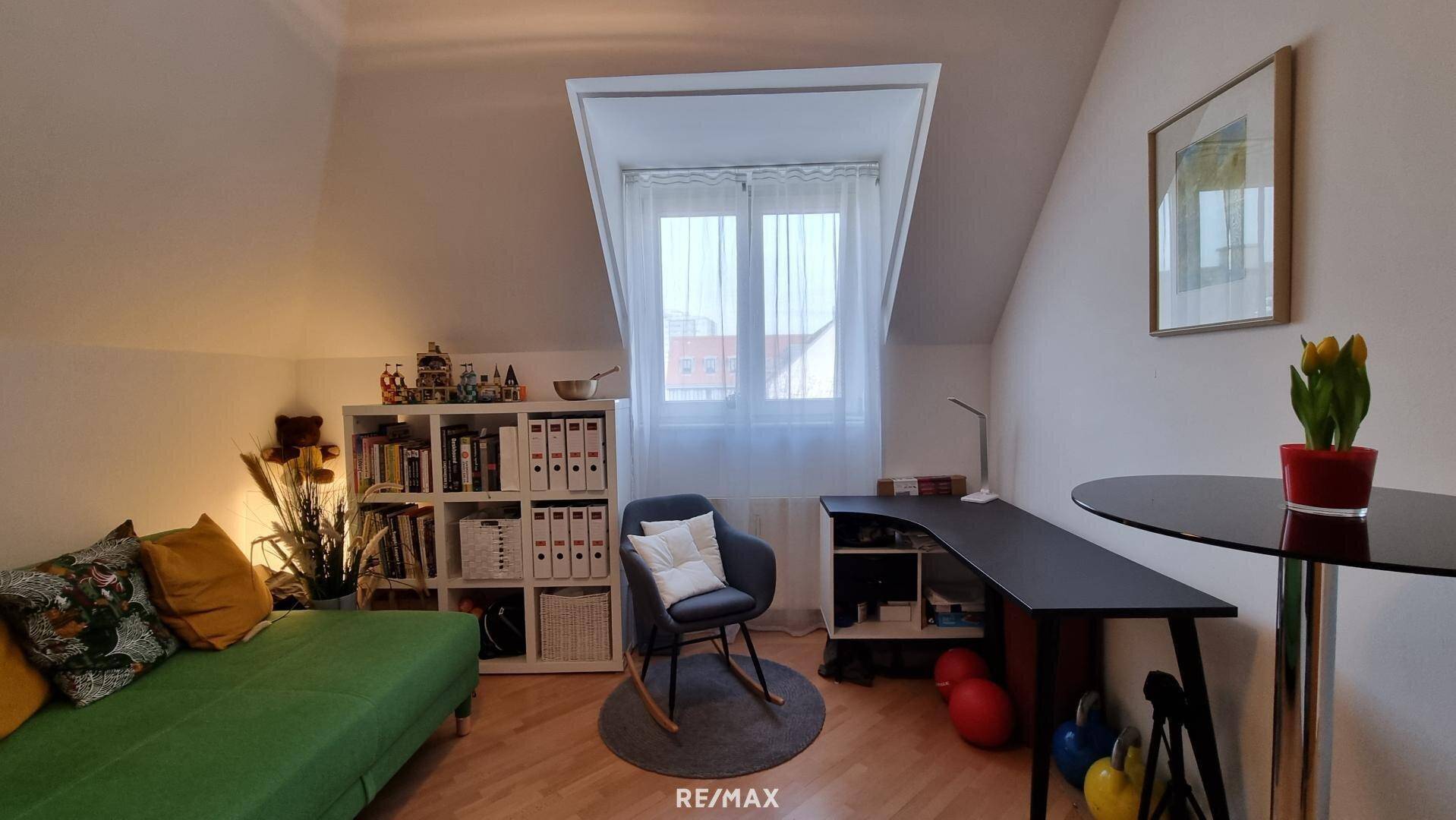 Helles Zimmer mit Schreibtisch, Bücherregal und gemütlichem Sofa unter der Dachschräge.