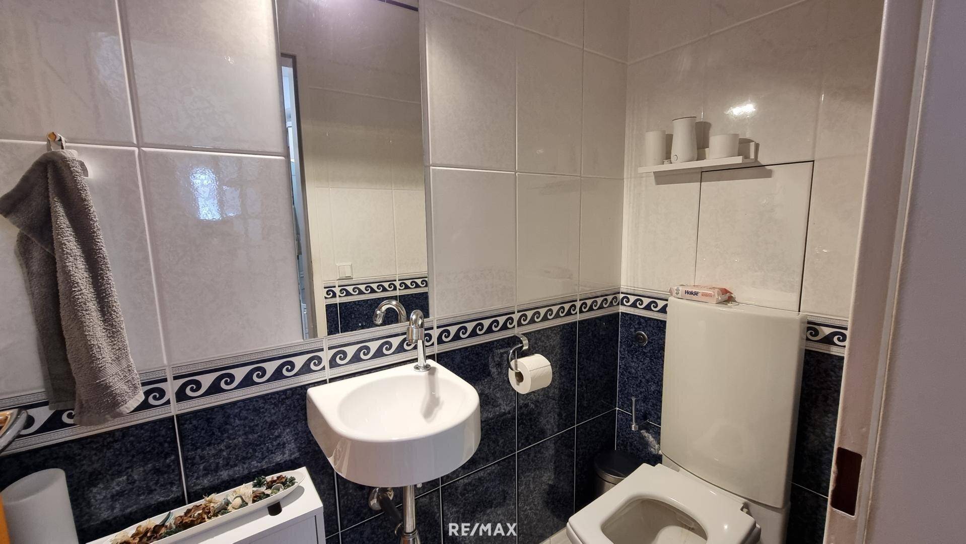 Kleines Gäste-WC mit Waschbecken, Toilette und blauen Fliesen im unteren Bereich.