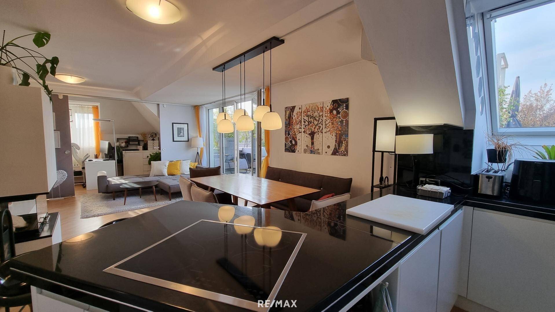 Moderne Küche mit Kochinsel und Essbereich, offen zum hellen Wohnzimmer mit Dachschrägen.