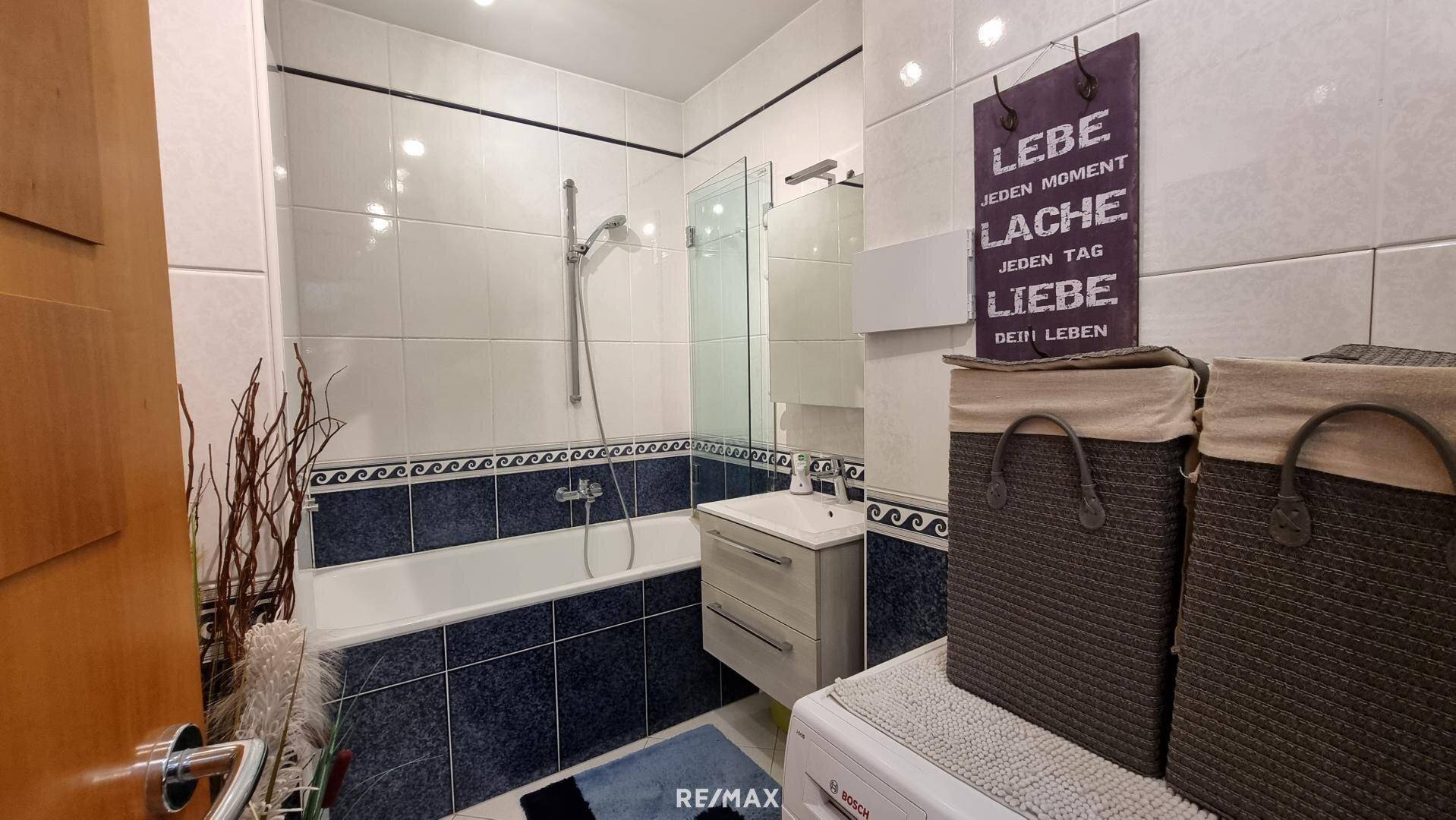 Badezimmer mit Badewanne, integrierter Dusche und Waschbecken, ausgestattet mit blauen Fliesen.