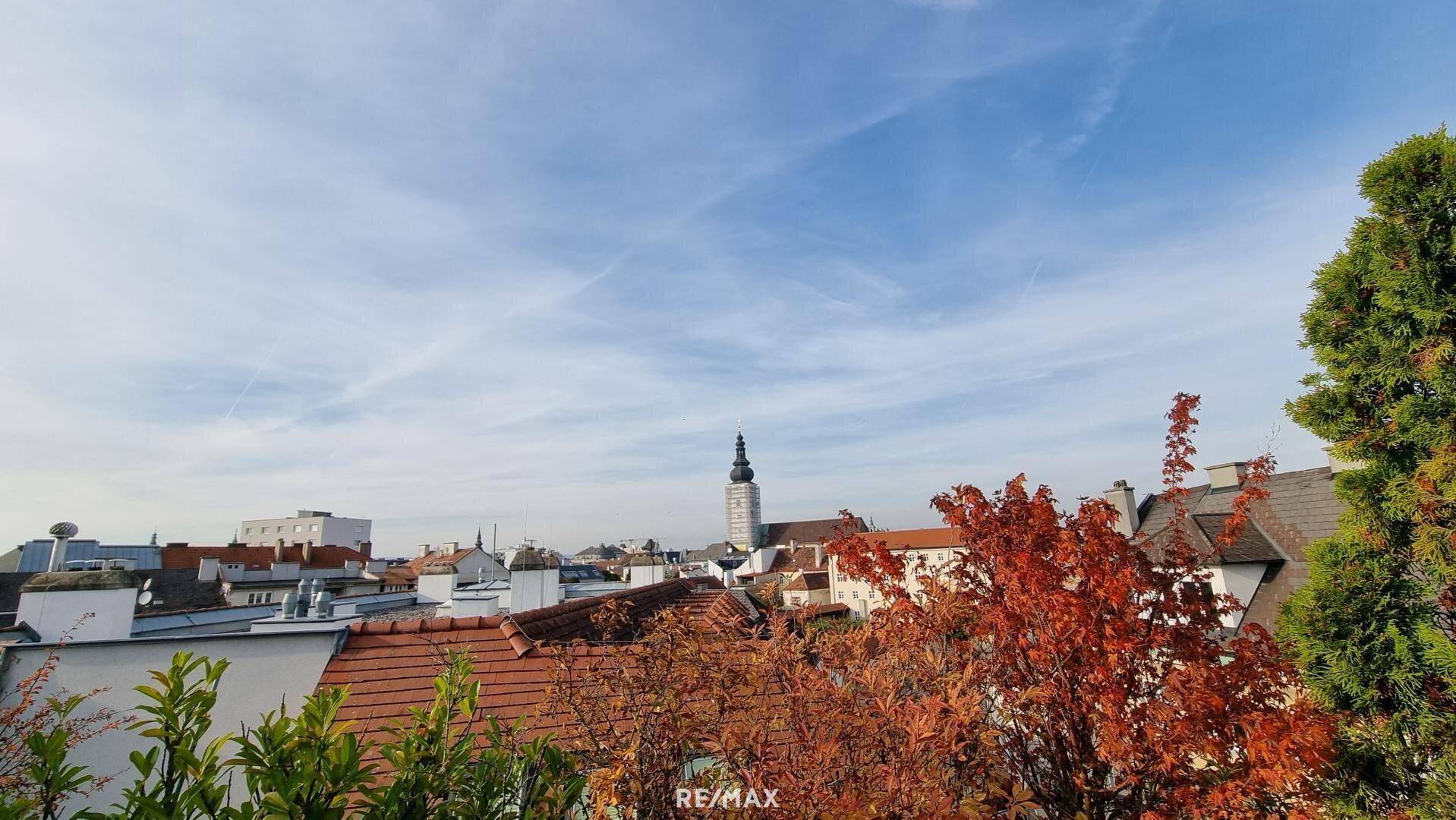 Weitläufiger Blick über die Dächer der Stadt mit historischem Kirchturm unter blauem Himmel.
