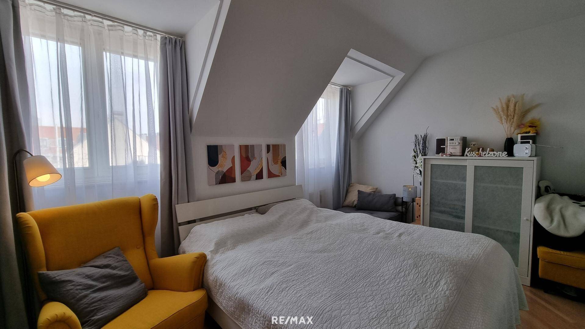 Gemütliches Schlafzimmer mit Doppelbett, Dachschrägen und großen Fenstern für viel Tageslicht.