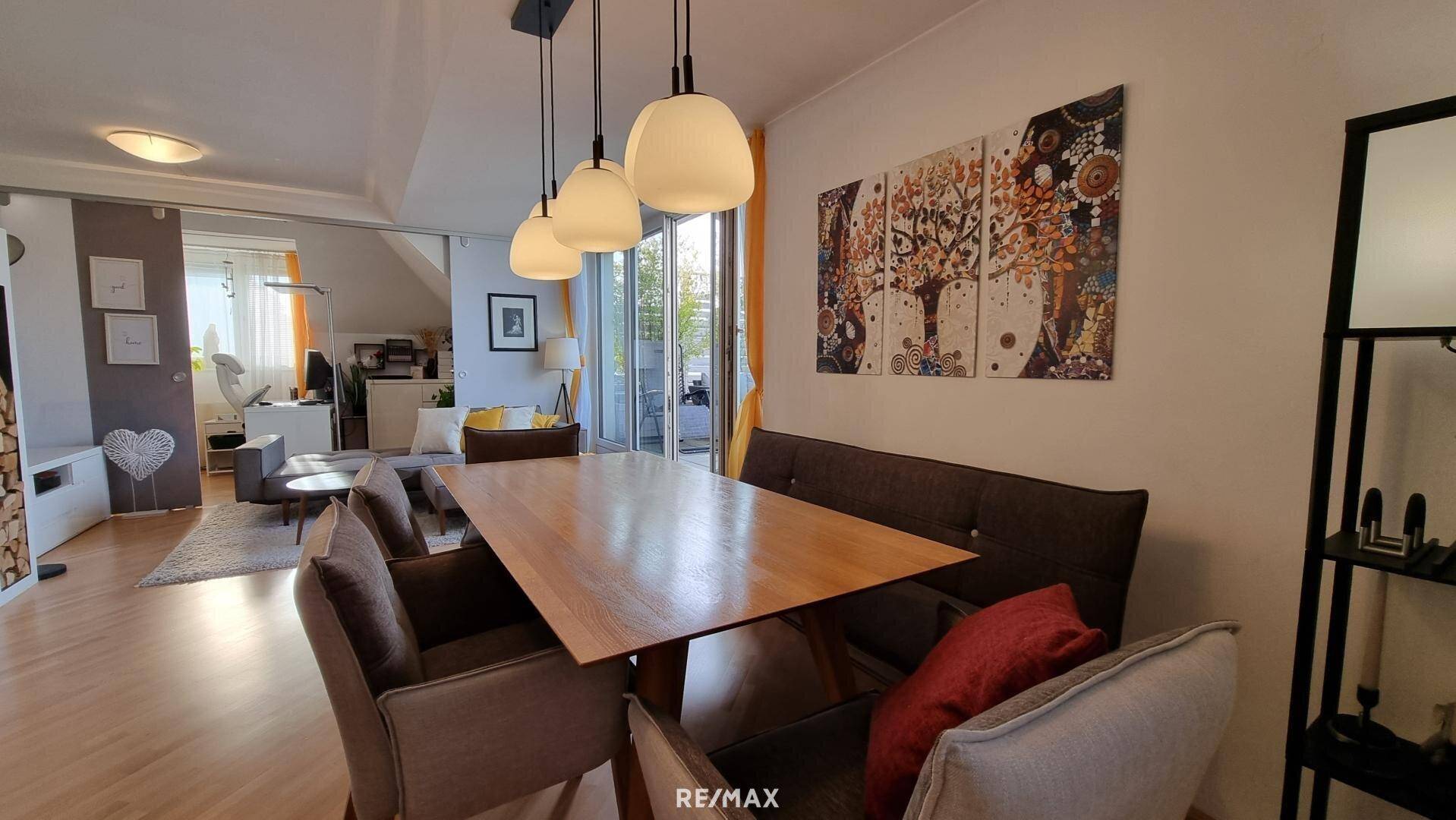 Gemütlicher Essbereich mit Holztisch und bequemen Stühlen, offen zum Wohnzimmer mit Kunstwerken.