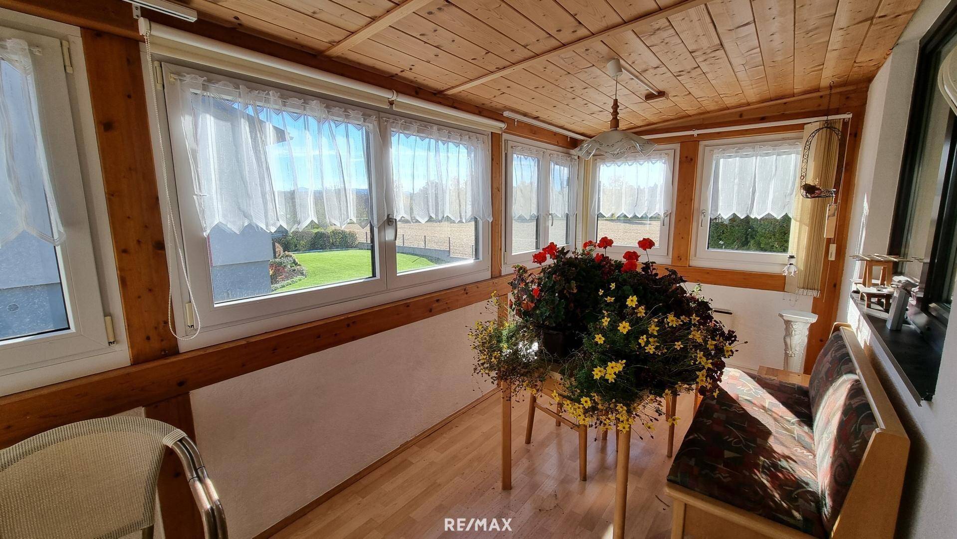 Lichtdurchfluteter Wintergarten mit Holzdecke, vielen Fenstern und Blick ins Grüne.