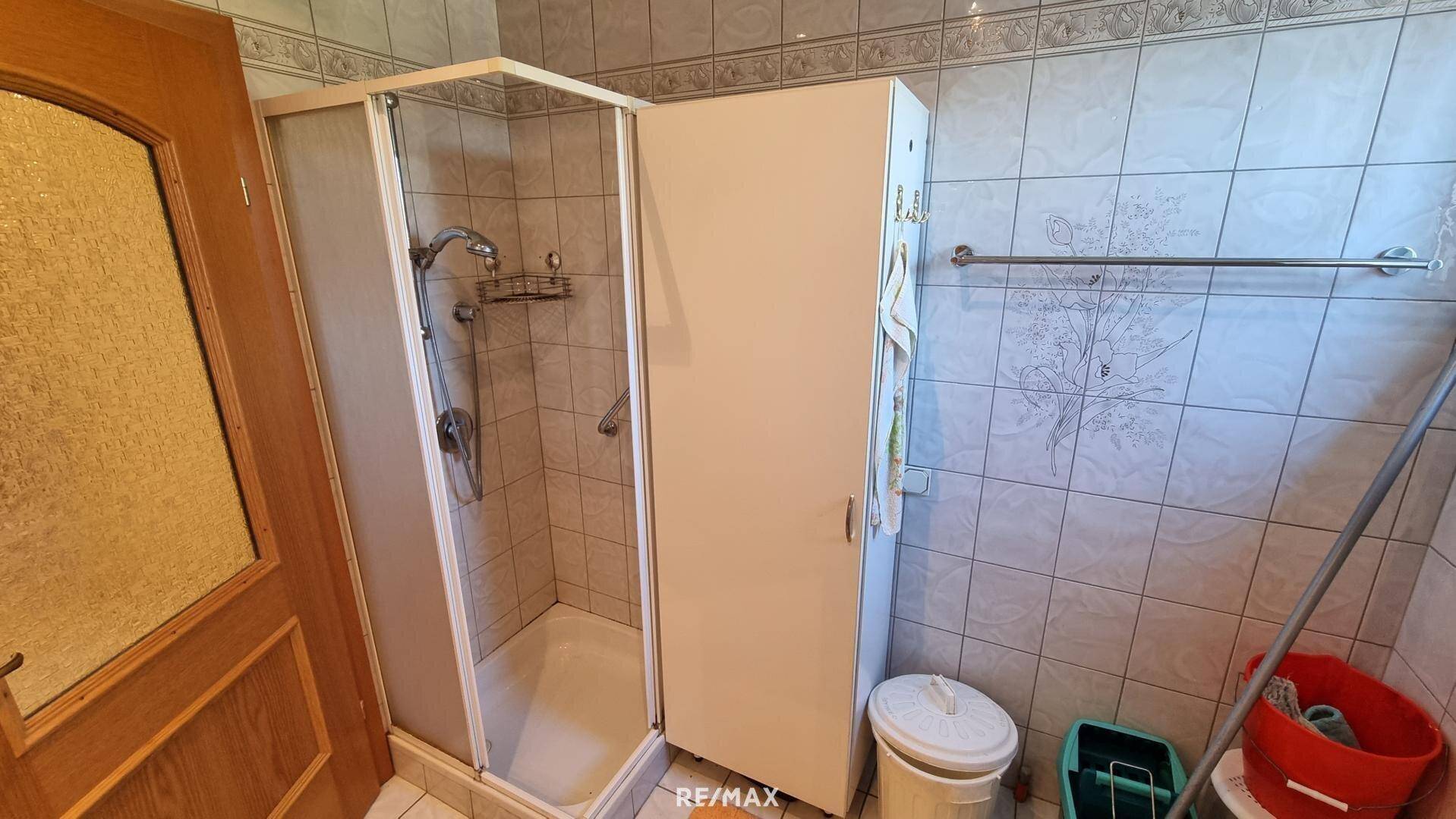 Badezimmer mit Duschkabine und Fliesen an Wänden und Boden.