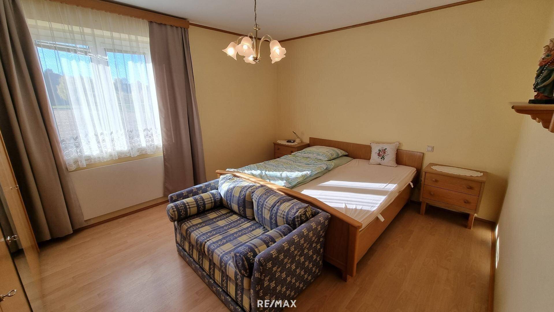 Gemütliches Schlafzimmer mit Holzbett, Sofa und Blick ins Grüne.