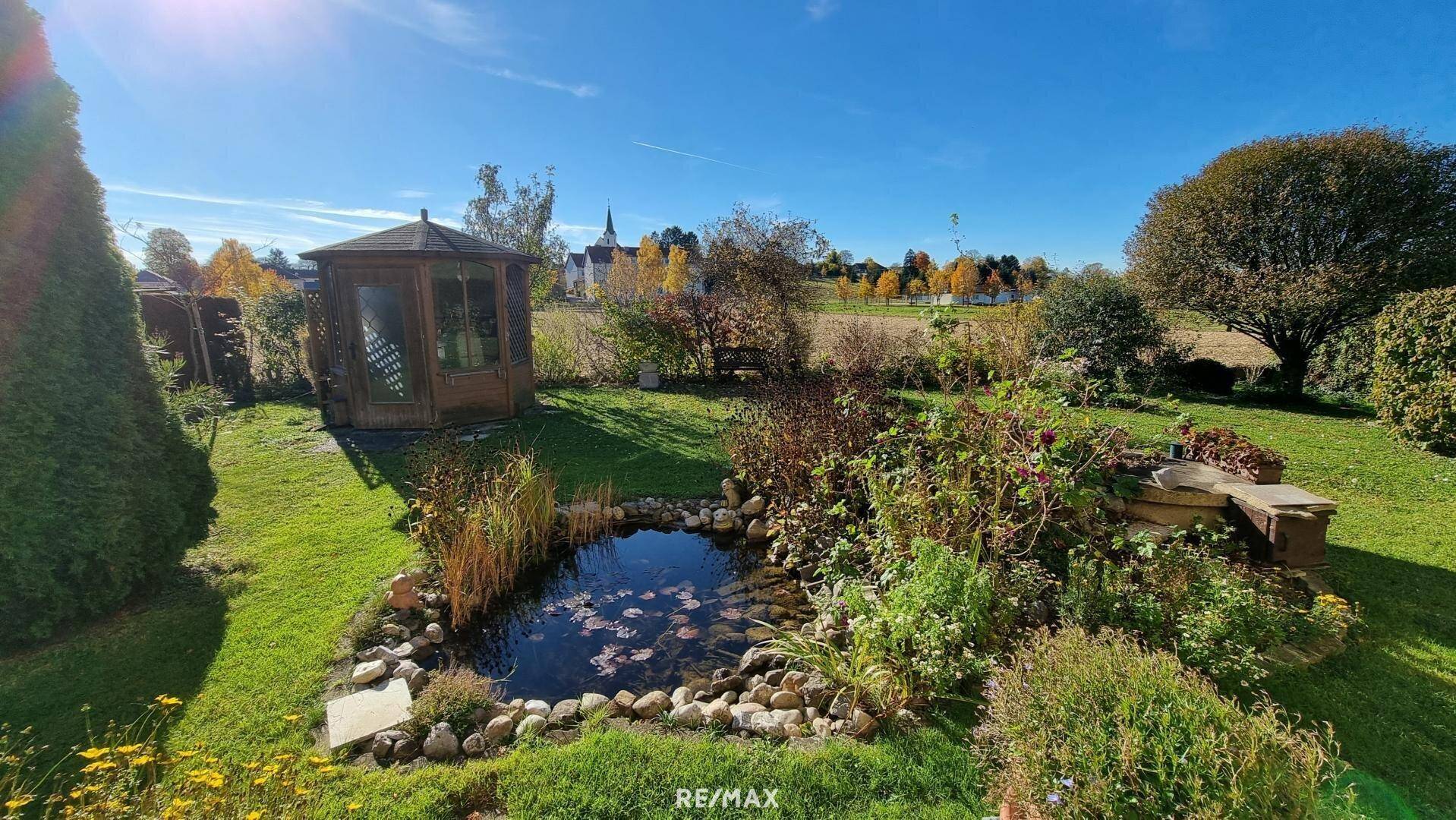 Idyllischer Garten mit Teich, Gartenlaube und weitem Blick über die Landschaft.